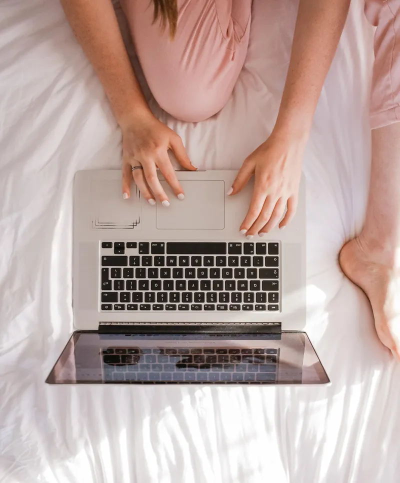 A woman is sitting on a bed using a laptop computer